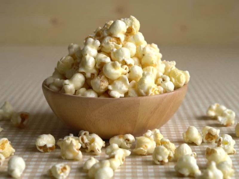 kokice u drvenoj činiji na stolu, nekoliko kokica rasutih pored